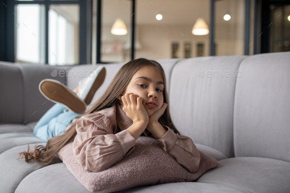 Sad little girl lying on a sofa at home. Stock Photo by Zinkevych D